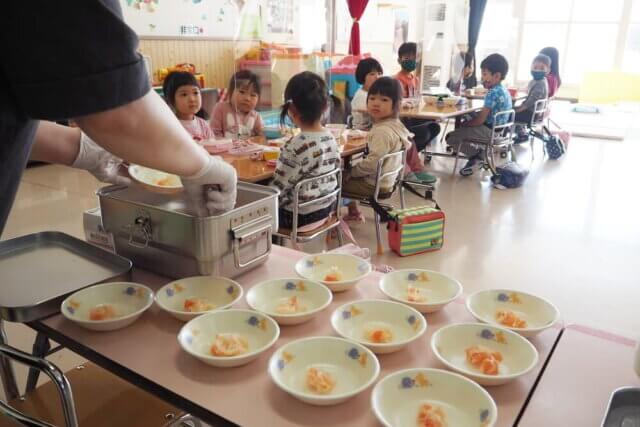 ダイコンの甘酢あえなどが皿に盛り付けられるのを見る園児