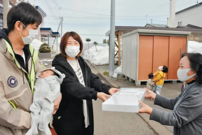 祝吉ちゃんを抱く貴博さん（左）と妻亜香さんに記念品を贈る緑町内会の役員