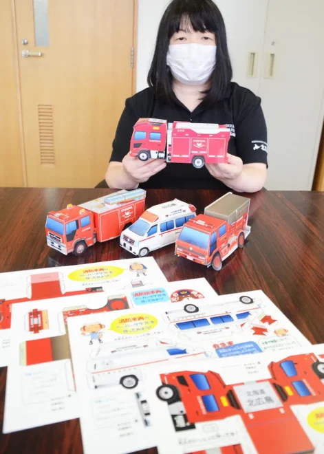 自身が制作した救急車や消防車のペーパークラフトを紹介する堀内さん