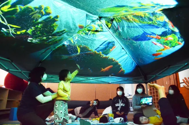 教室で布に映し出された熱帯魚の映像を見る児童ら