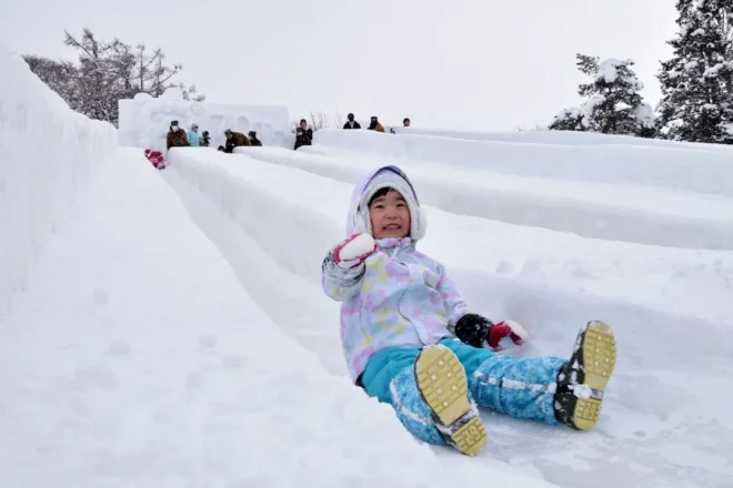 雪んこまつりで雪の滑り台を元気よく滑り降りる子どもたち