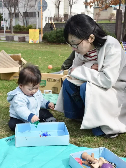 母親の沖野優子さん（右）に見守られながら、公園の芝生に座って遊ぶ叶志郎ちゃん