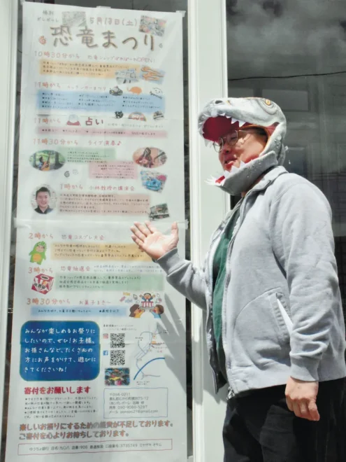 恐竜のかぶり物をつけながら、むかわ町穂別で初めて開く「恐竜まつり」について説明する宮崎さん