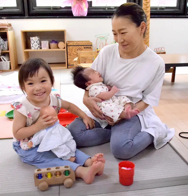 黒木陽子さんが生後３カ月の琶賀ちゃんを抱く横で、同じように人形を抱く琶梛ちゃん