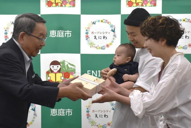 原田裕市長（左）から木でできた玩具を受け取った佐藤さん親子