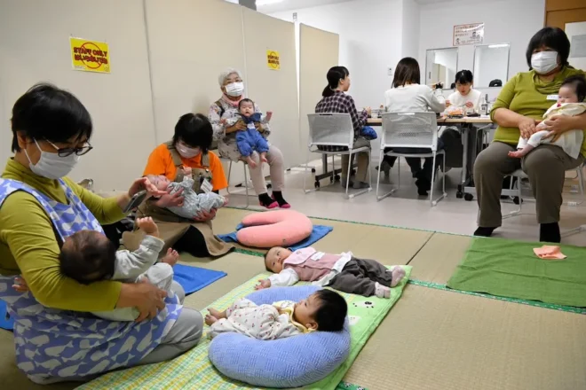 母親同士で交流する中、赤ん坊をあやす助産師たち
