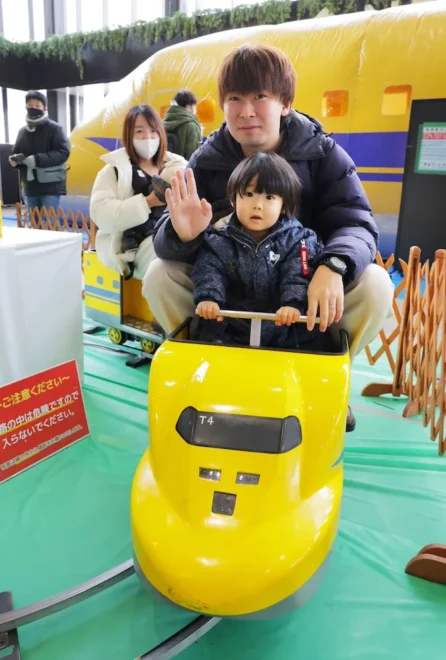 ふわふわ遊具の前の動くミニドクターイエローに乗る親子連れ(岩崎勝撮影)